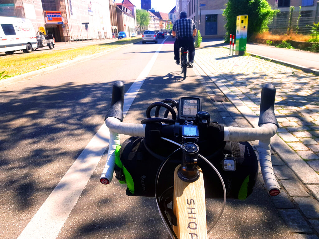 An look on the packed steer with the type of the bicycle visible on the wooden top tube. Bicycling on the road in an city with in the front another cyclist.
