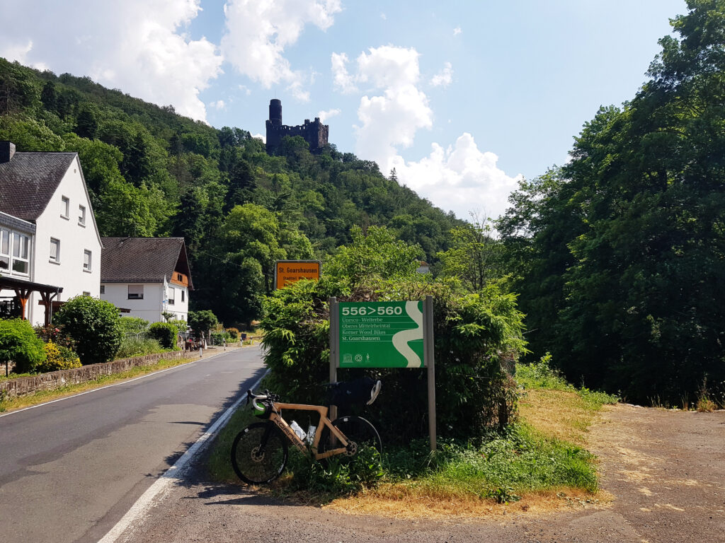 The wooden road bicycle posed down a sign of Unesco heritage on the side of the road, with a castle on the background on the hill.